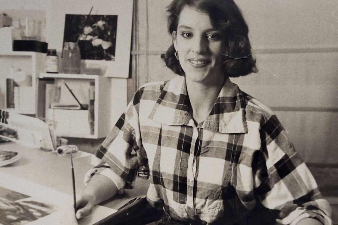 Josée jeune, en chemise à carreaux, assise à une table de travail couverte d'images.