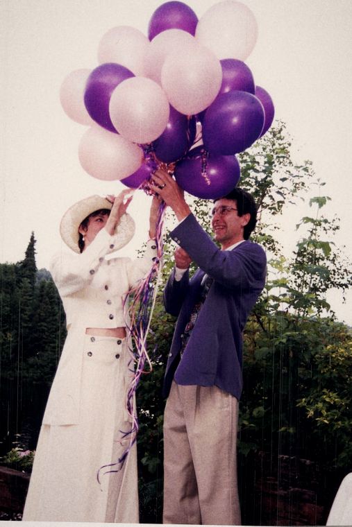Josée en tailleur crème et chapeau, lâchant une grappe de ballons mauves et blancs.