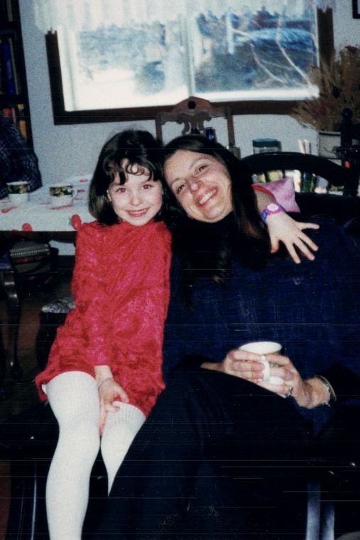 Josée dans un fauteuil, une tasse à la main, une fillette en robe rouge à ses côtés.