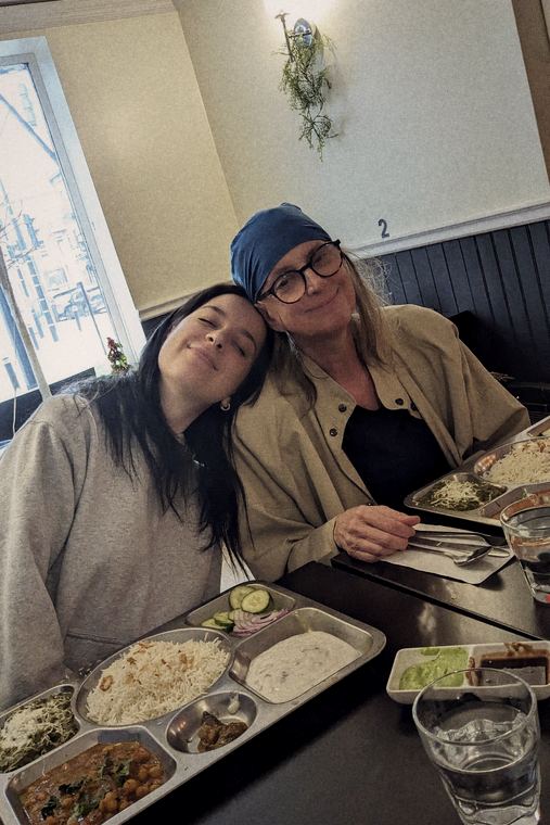 Josée en foulard bleu et veste beige, la tête appuyée contre celle de sa fille, au restaurant.